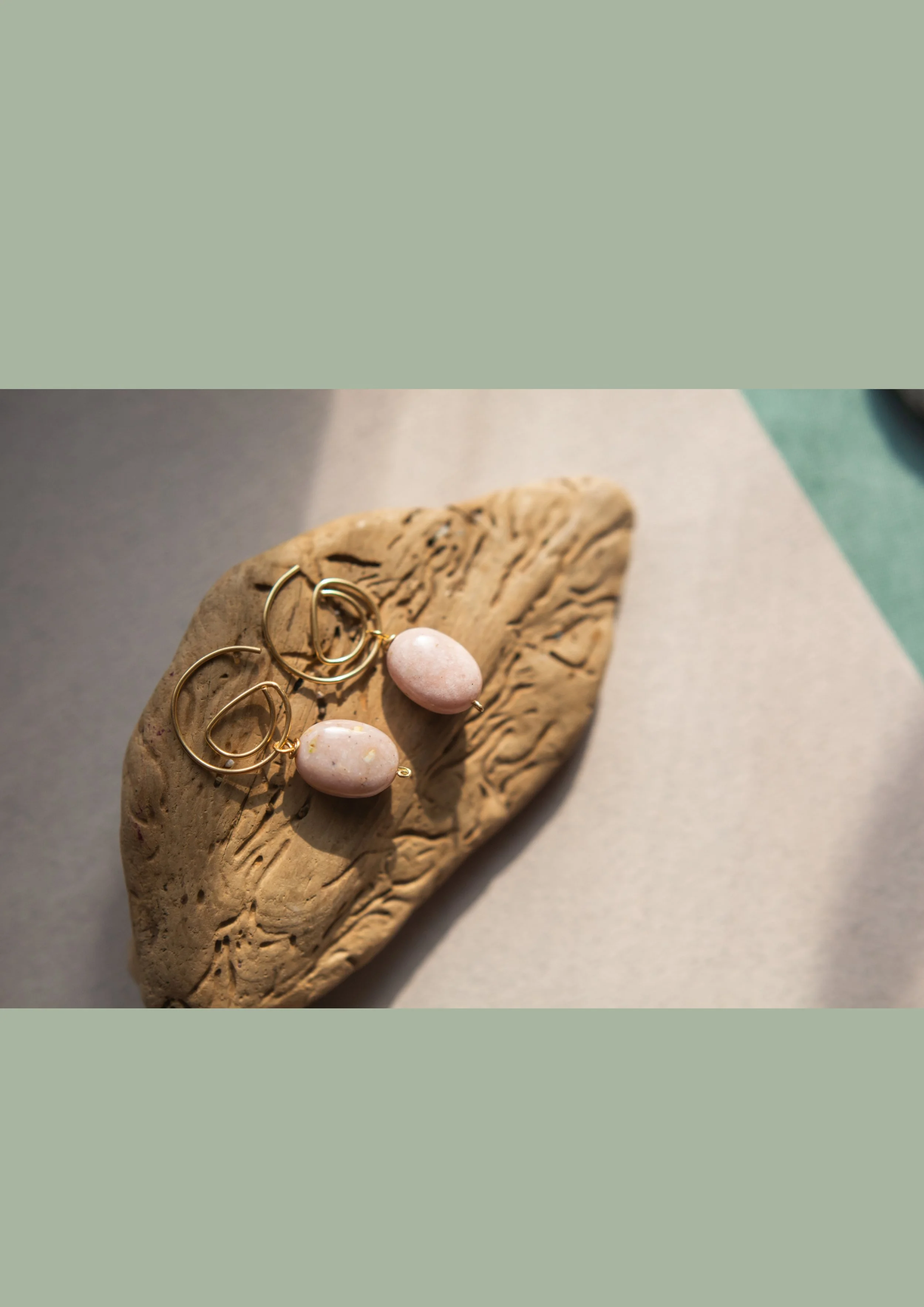 Close-up of a decorative piece with pink and gold earrings on a textured, beige, boat-shaped ceramic dish on a neutral surface.