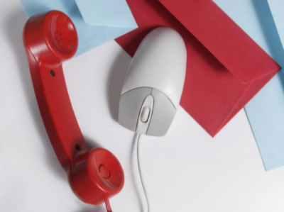 Red vintage telephone, white computer mouse, and red and blue paper on a desk.