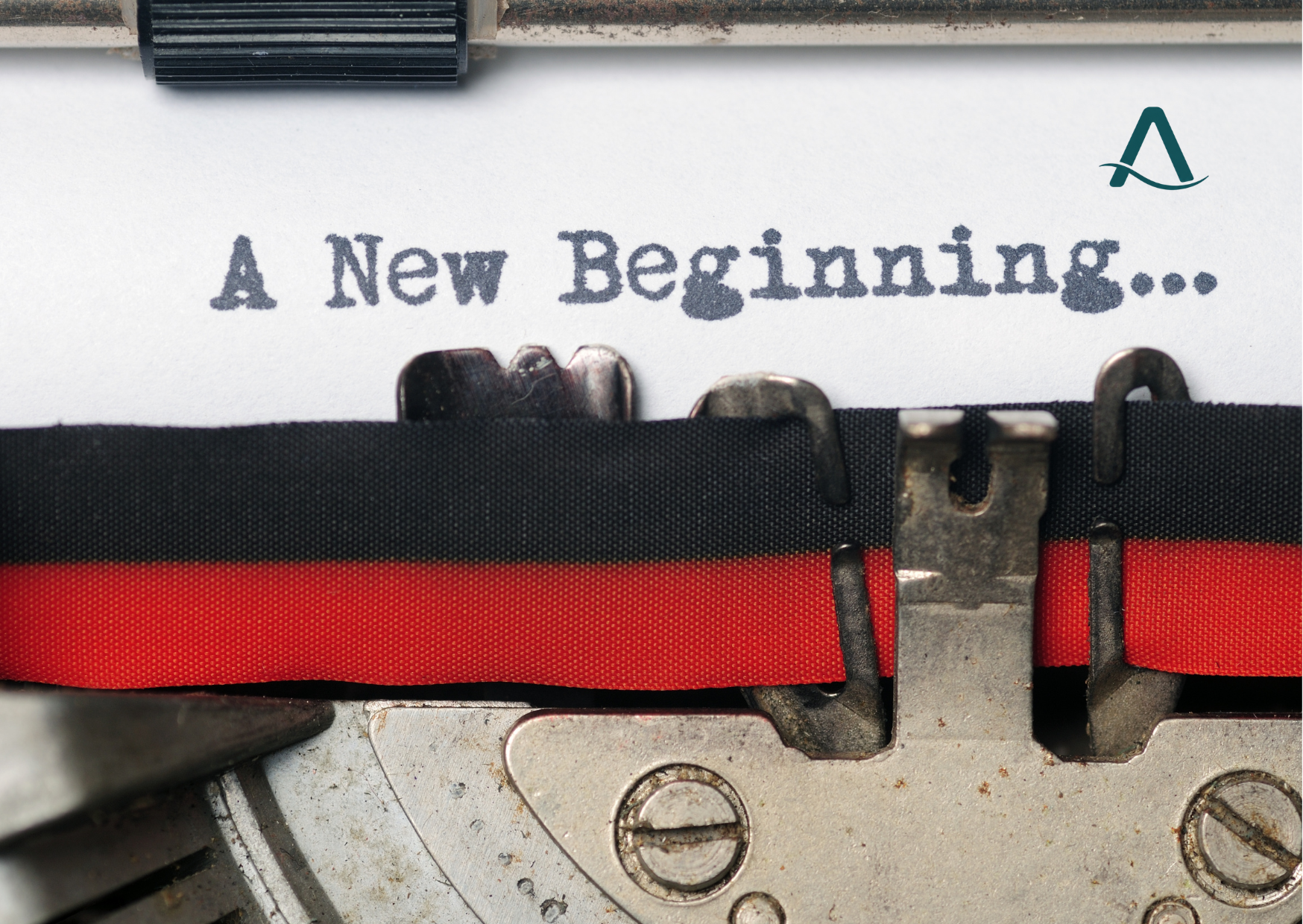 Close-up of a typewriter with the phrase 'A New Beginning...' typed on white paper. The typewriter's black and red ribbon is visible, along with metal typebars and screws.