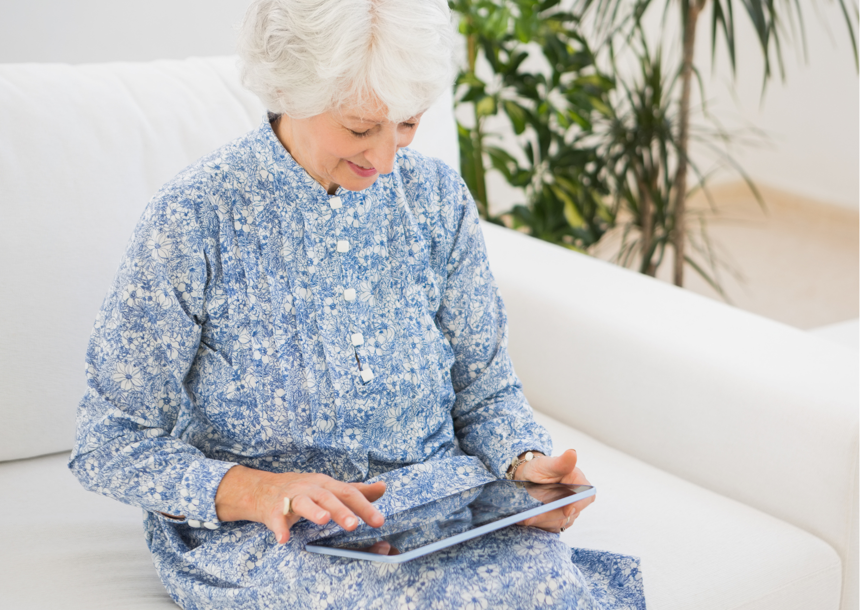 Lady in a blue dress sitting on sofa and looking at her tablet
