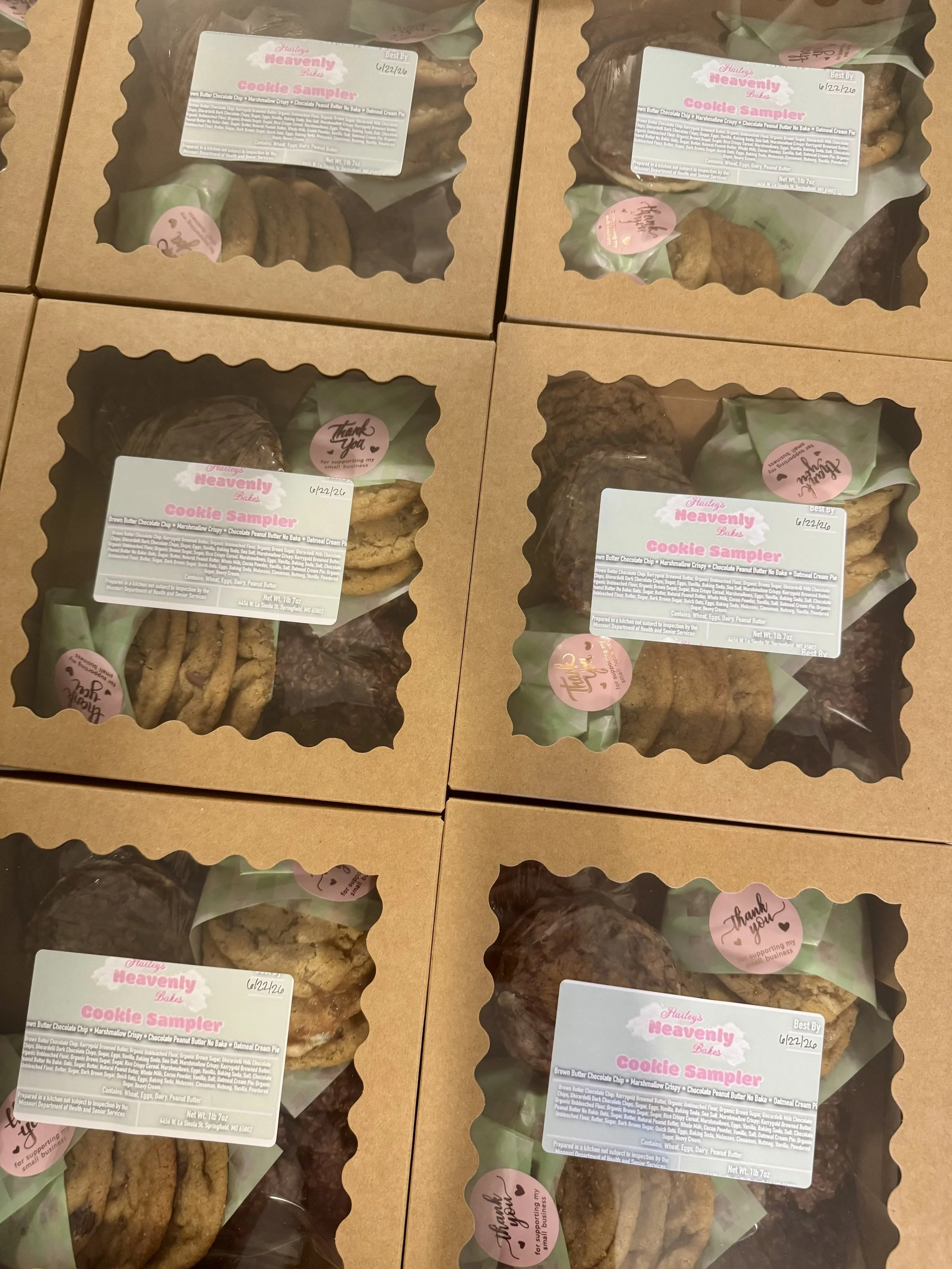 Four boxes of cookies with clear plastic windows showing assorted cookies inside. Each box label reads 'Hailey's Heavenly Bakes Cookie Sampler,' with a list of cookie types and ingredients. The boxes are arranged in a grid pattern.