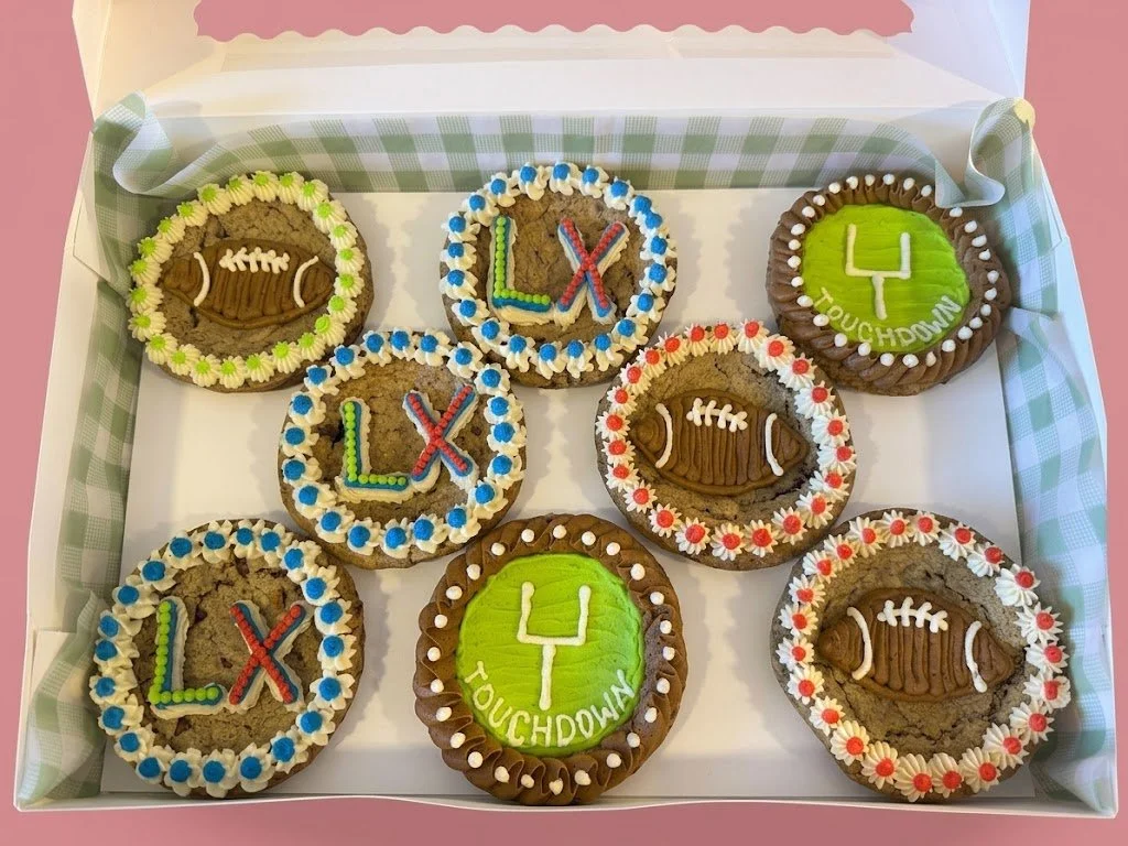 A box of themed cookies for a football game, decorated as footballs with borders of colored icing, some with the words 'L,