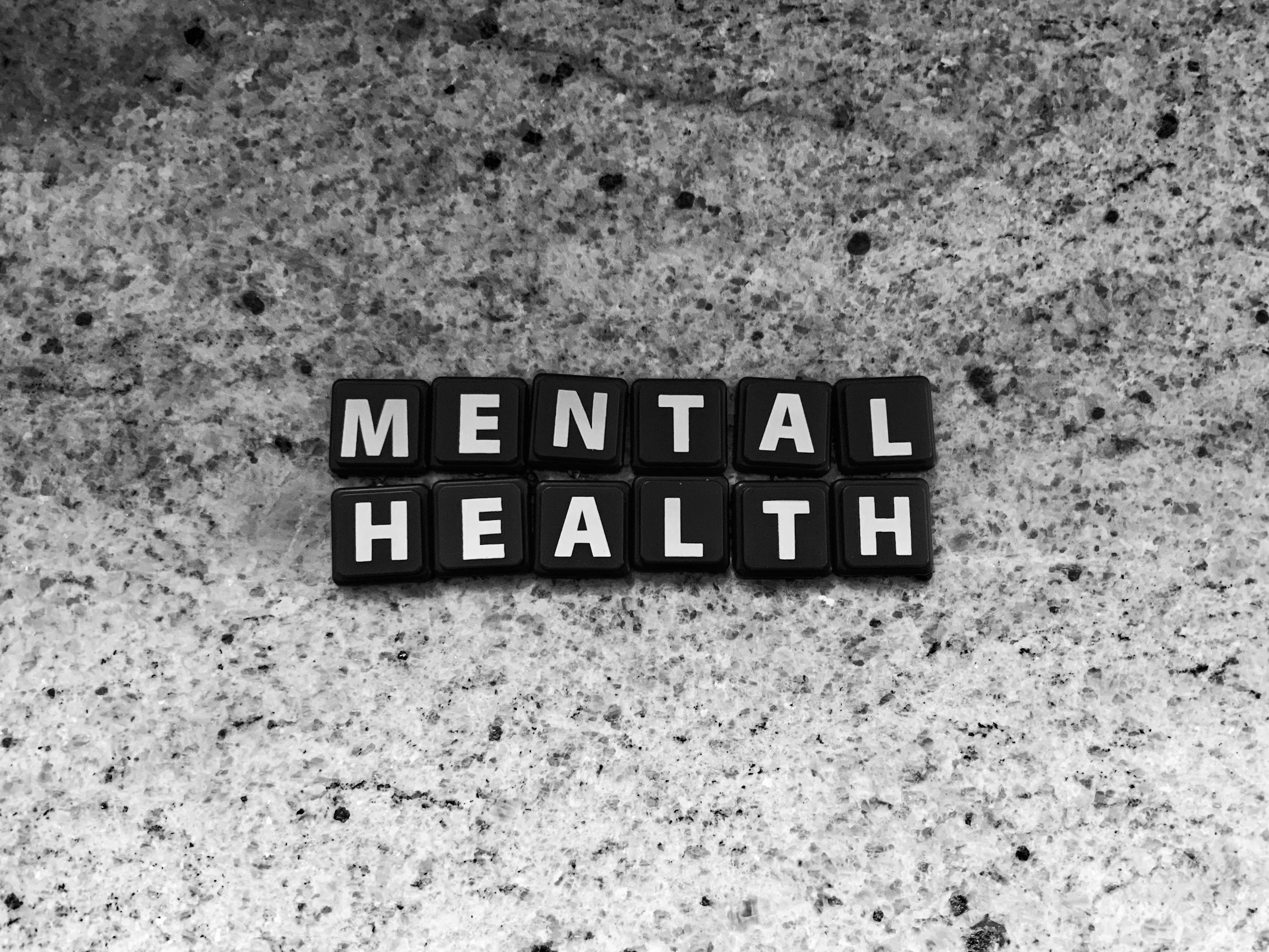 Black tiles with white letters spelling out 'MENTAL HEALTH' on a speckled gray countertop.