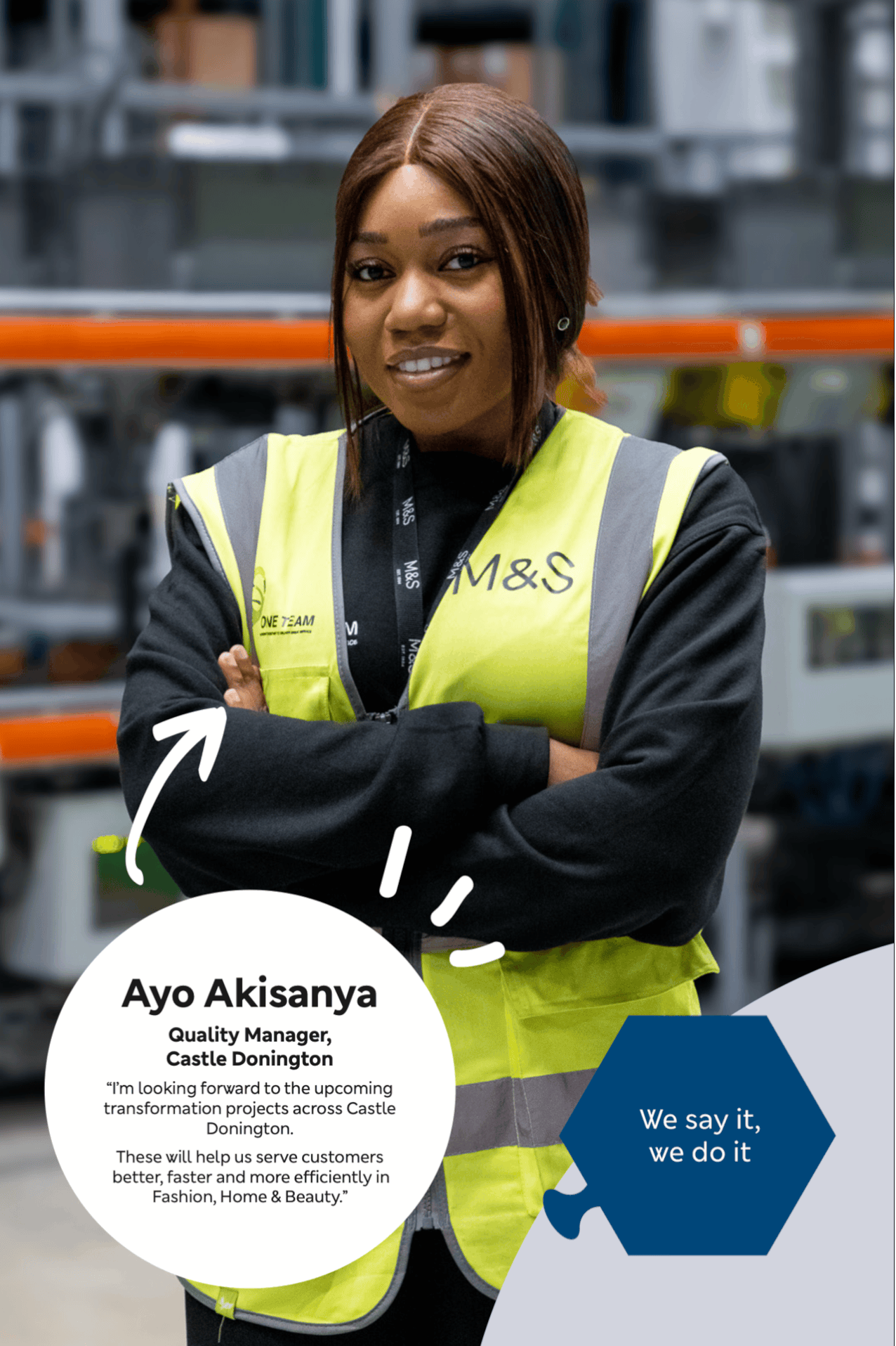 Portrait of a woman in a yellow safety vest with 'M&S' logo, standing with arms crossed in a warehouse with shelves.