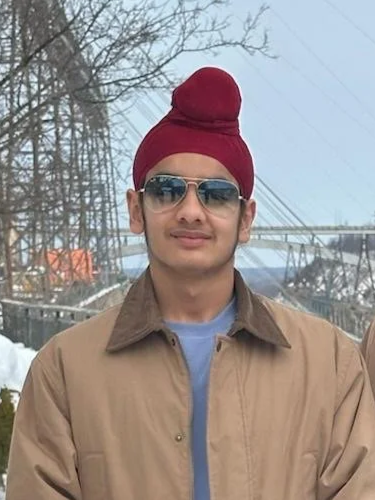 Young man wearing sunglasses, a red turban, and a beige jacket outdoors during winter, with power lines and snow in the background.