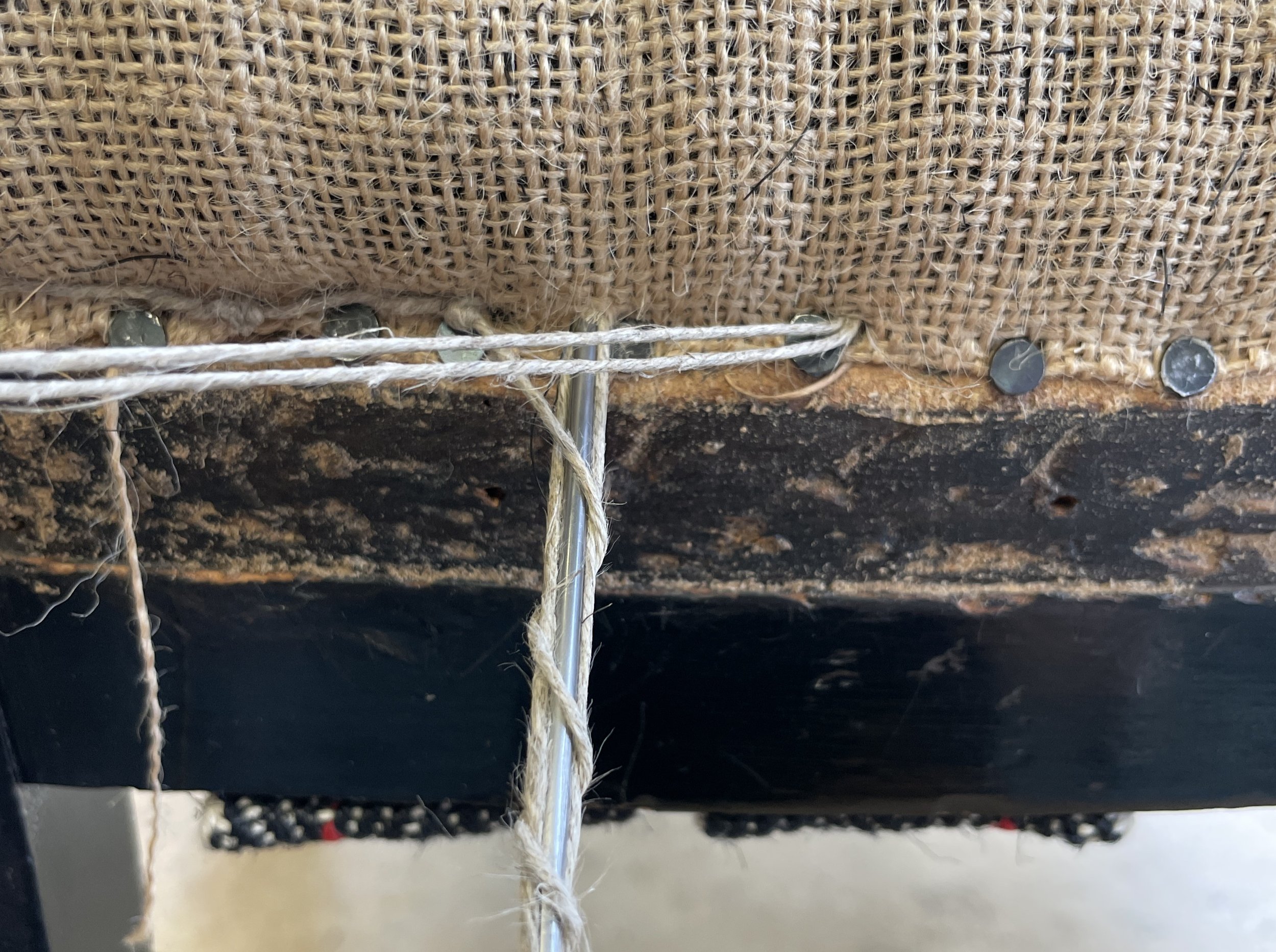 Close-up detail of blind stitching, a traditional method of edging a chair. The needle disappears into the hessian the top thread is pulled taught and the under-thread is wound three times around the needle.