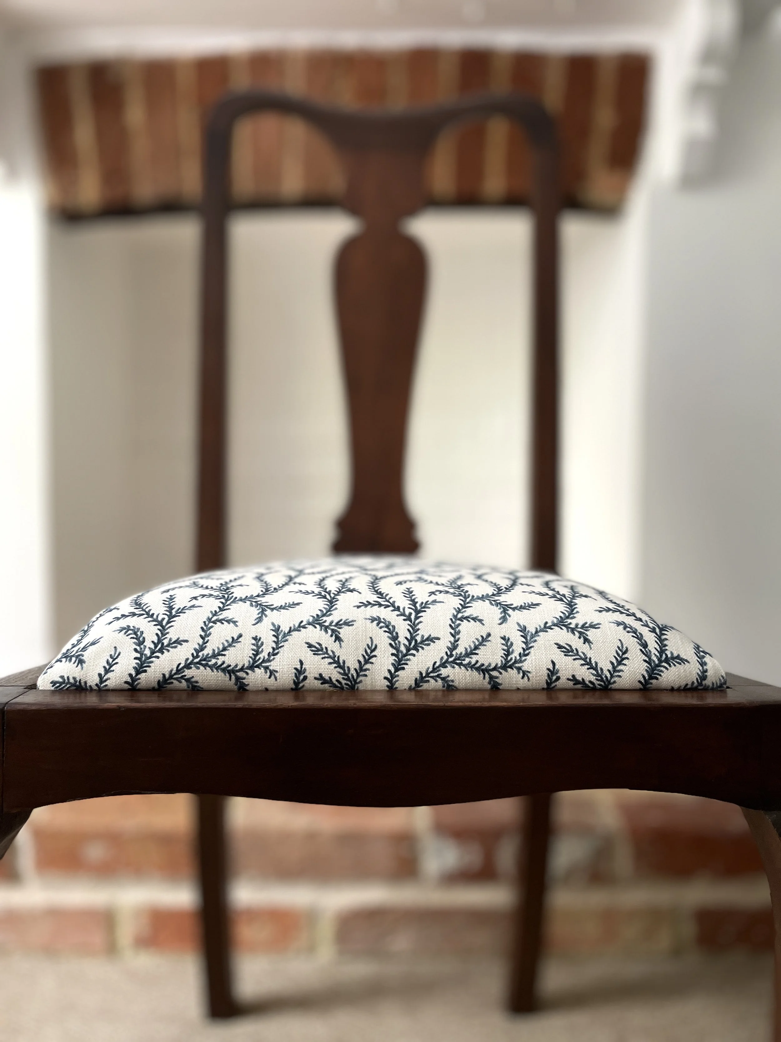 close up of front of dining chair with newly upholstered seat. the fabric is fresh off-white with delicate ink-blue tendrils.