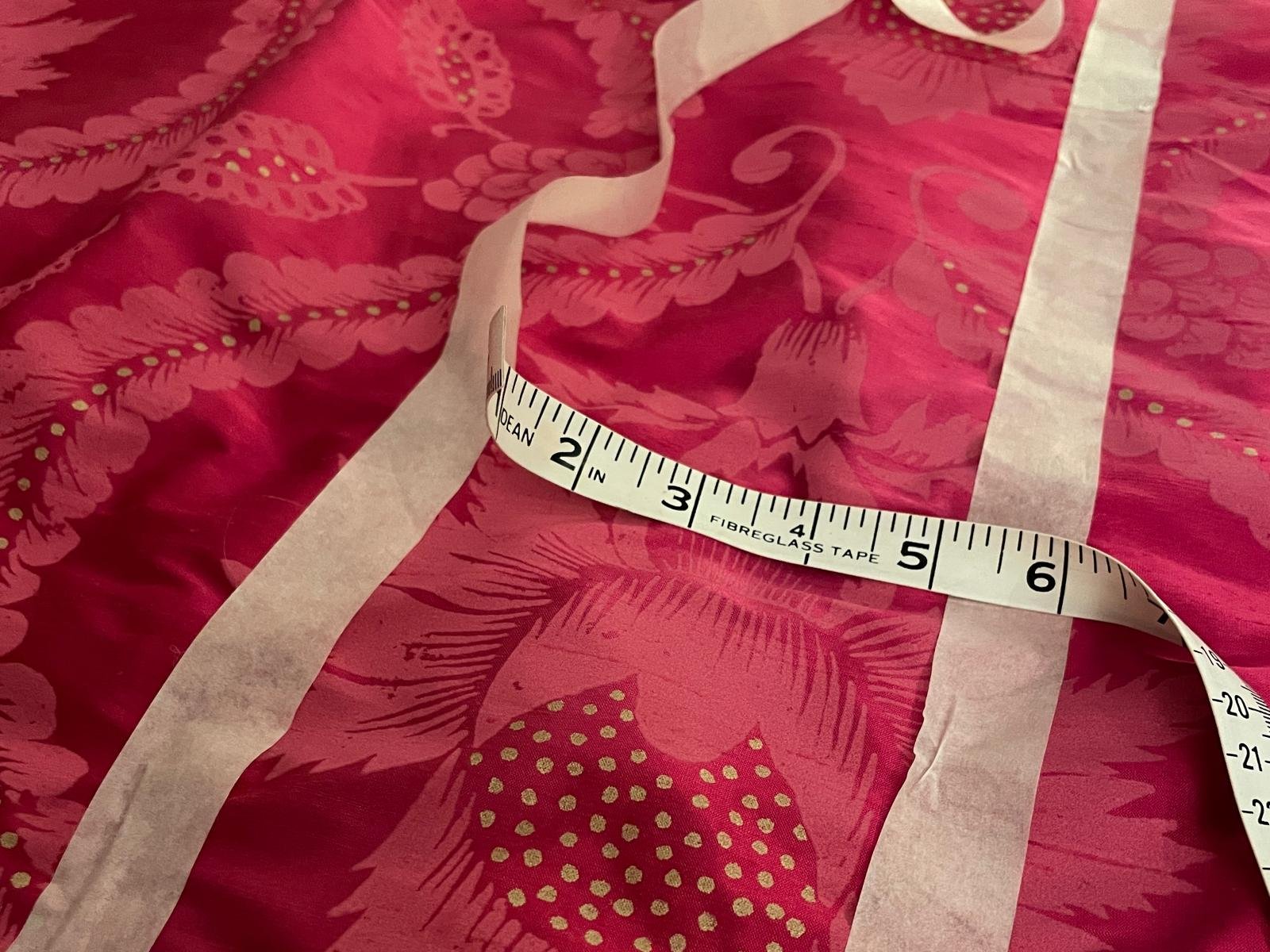 Pink silk coverlet with pale pink and gold flowers. It is marked out with masking tape and the tape measure curves across the fabric.