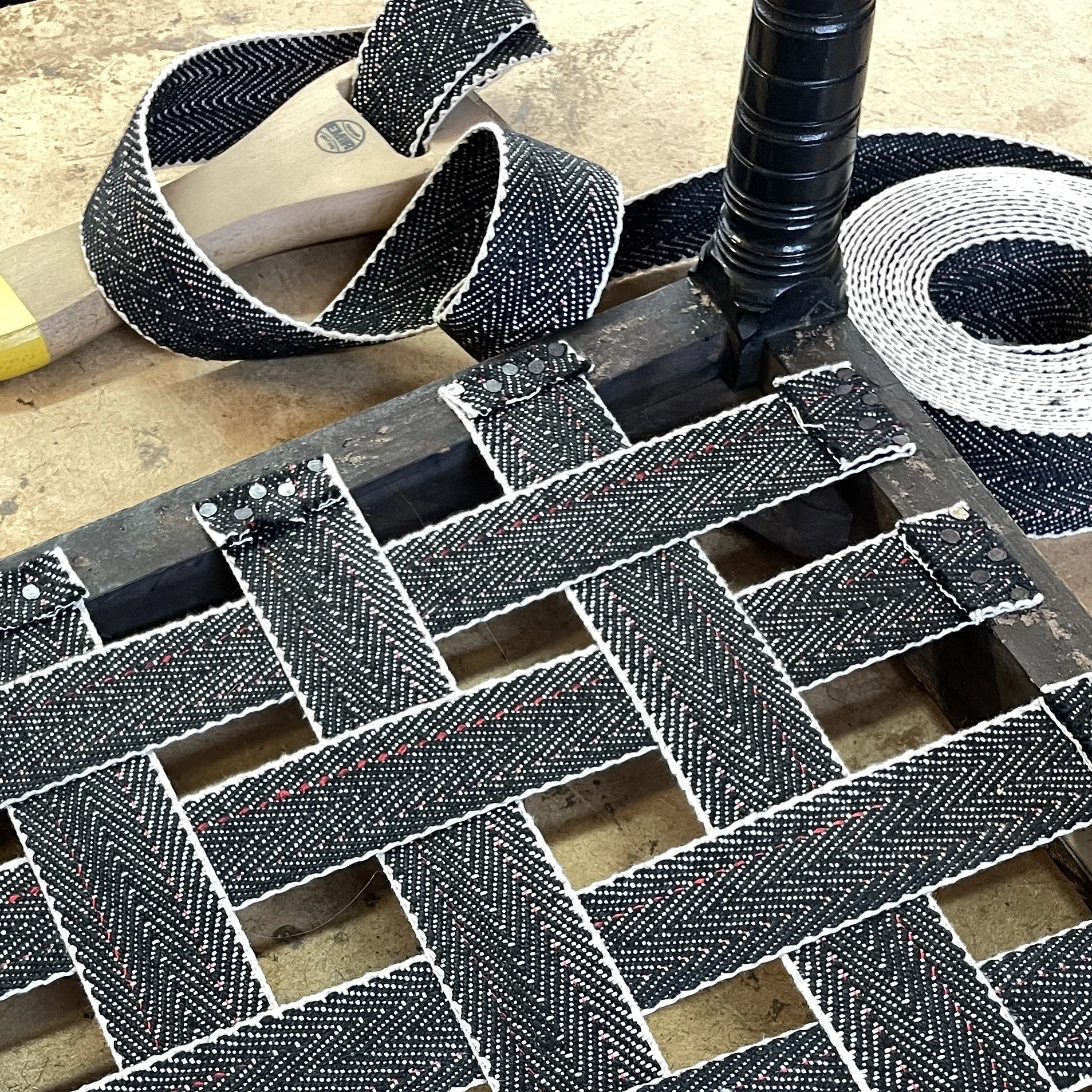 Criss cross black and white webbing over the base of a seat frame with the webbing still coiled in the webbing stretch on the table behind.