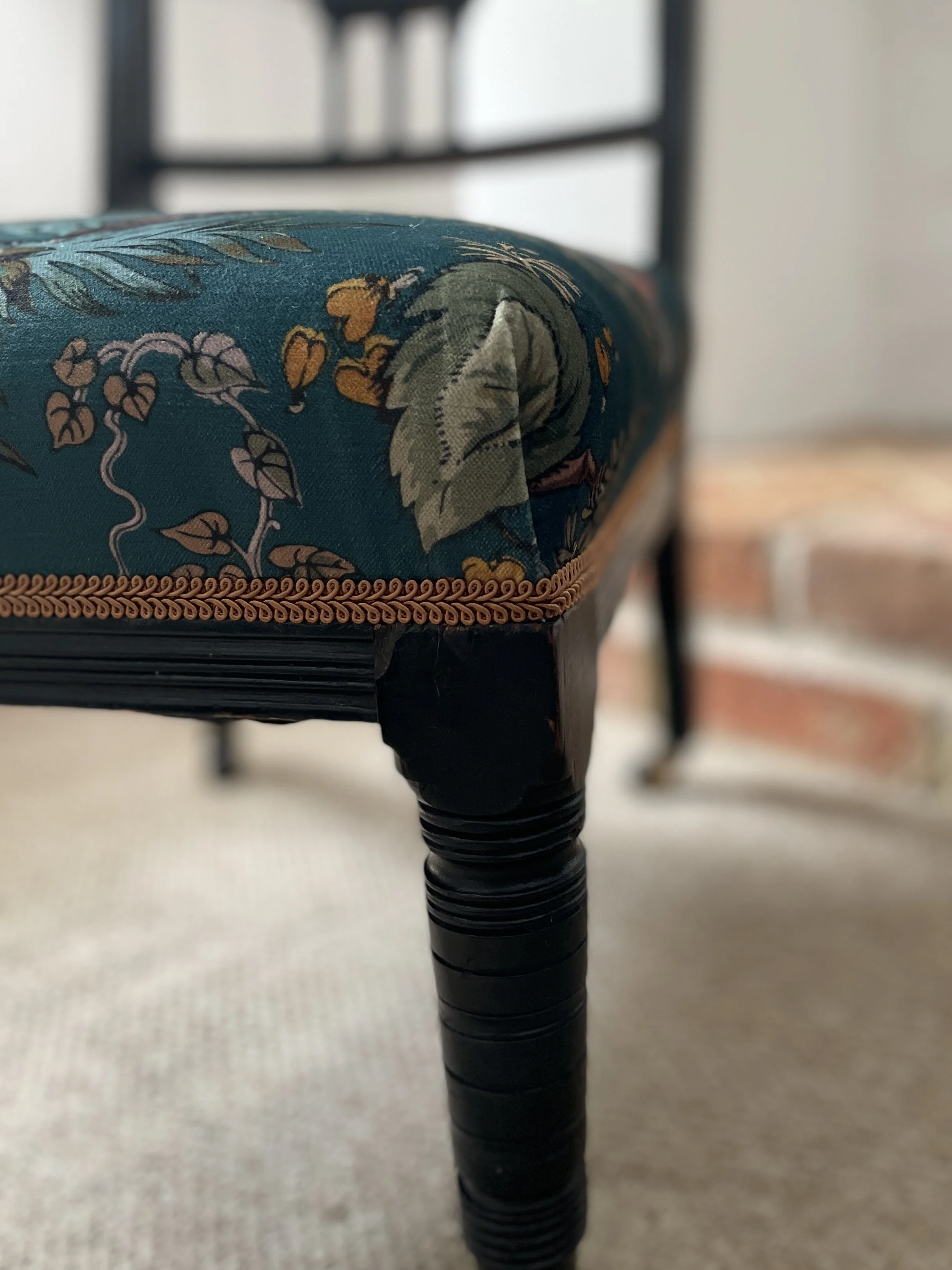 Corner detail of a nursing chair upholstered in emerald green fabric a yellow leaf is furled over the corner.