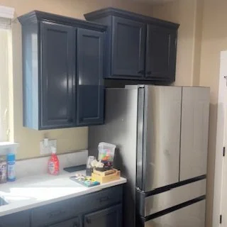 Kitchen with dark blue cabinets, a stainless steel refrigerator, and a white countertop. There are cleaning supplies and miscellaneous items on the counter.