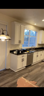 Kitchen with white cabinets, a double sink, window above the sink, and countertop appliances, with laminate flooring.