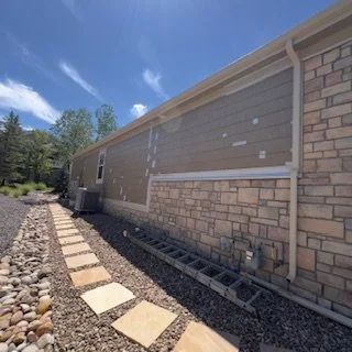 Side view of a modern building with brick and siding walls, a gravel pathway with stepping stones, and a clear blue sky.