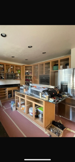 Empty kitchen with wooden cabinets, a kitchen island, and a black countertop, cluttered with various items.