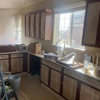Kitchen with wooden cabinets, a window, a sink, and various bottles and items on the countertop.