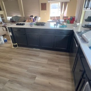 View of a kitchen with blue cabinets, white countertops, and a window letting in natural light. Items like a potted plant and kitchen supplies are on the counter.
