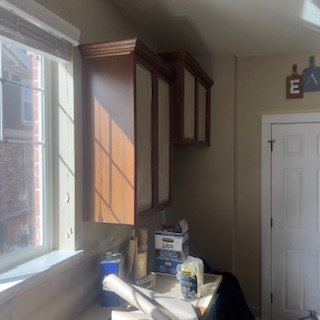Kitchen with wooden cabinets, a window letting in sunlight, and various items on the counter including a paper towel roll and containers.