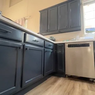 Kitchen with dark blue cabinets, a window, and a built-in dishwasher.