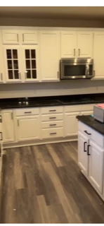 Kitchen with white cabinets, black countertop, stainless steel microwave, and dark wood flooring.