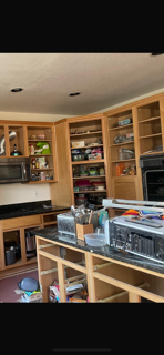 View of empty kitchen cabinets and countertop with various items, including a dish drying rack, a microwave, and some scattered papers.
