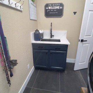 Laundry room with a sink, dark cabinet, and wall decor including welcome sign and hooks.