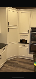 White kitchen cabinets with black handles, built-in oven, and a corner cabinet with a cutout section