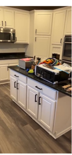 Kitchen island with various items including books, documents, and electronic devices on top; white cabinets and stainless steel appliances in the background.