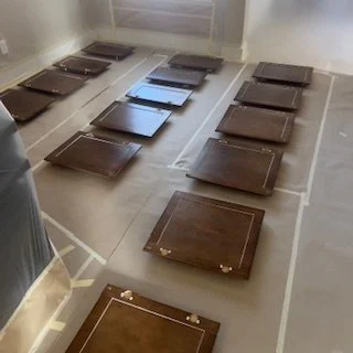 Multiple brown picture frames laid face down on a wooden floor inside a room.