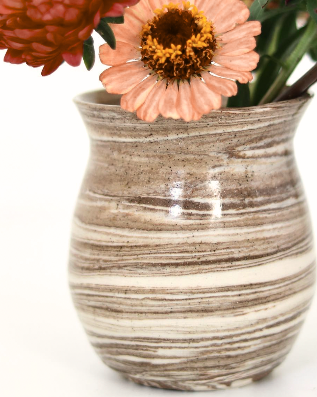 Close-up of a ceramic vase with beige, brown, and white horizontal stripes, holding peach and pink flowers.