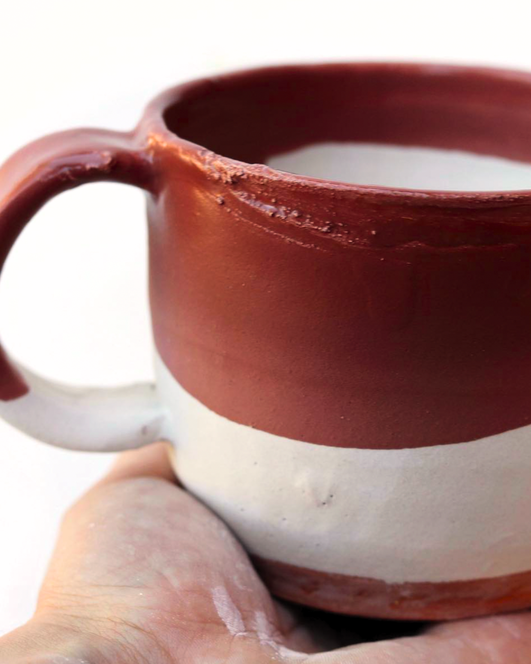 Close-up of a ceramic mug with a two-tone design, featuring a maroon upper half and an off-white lower half.