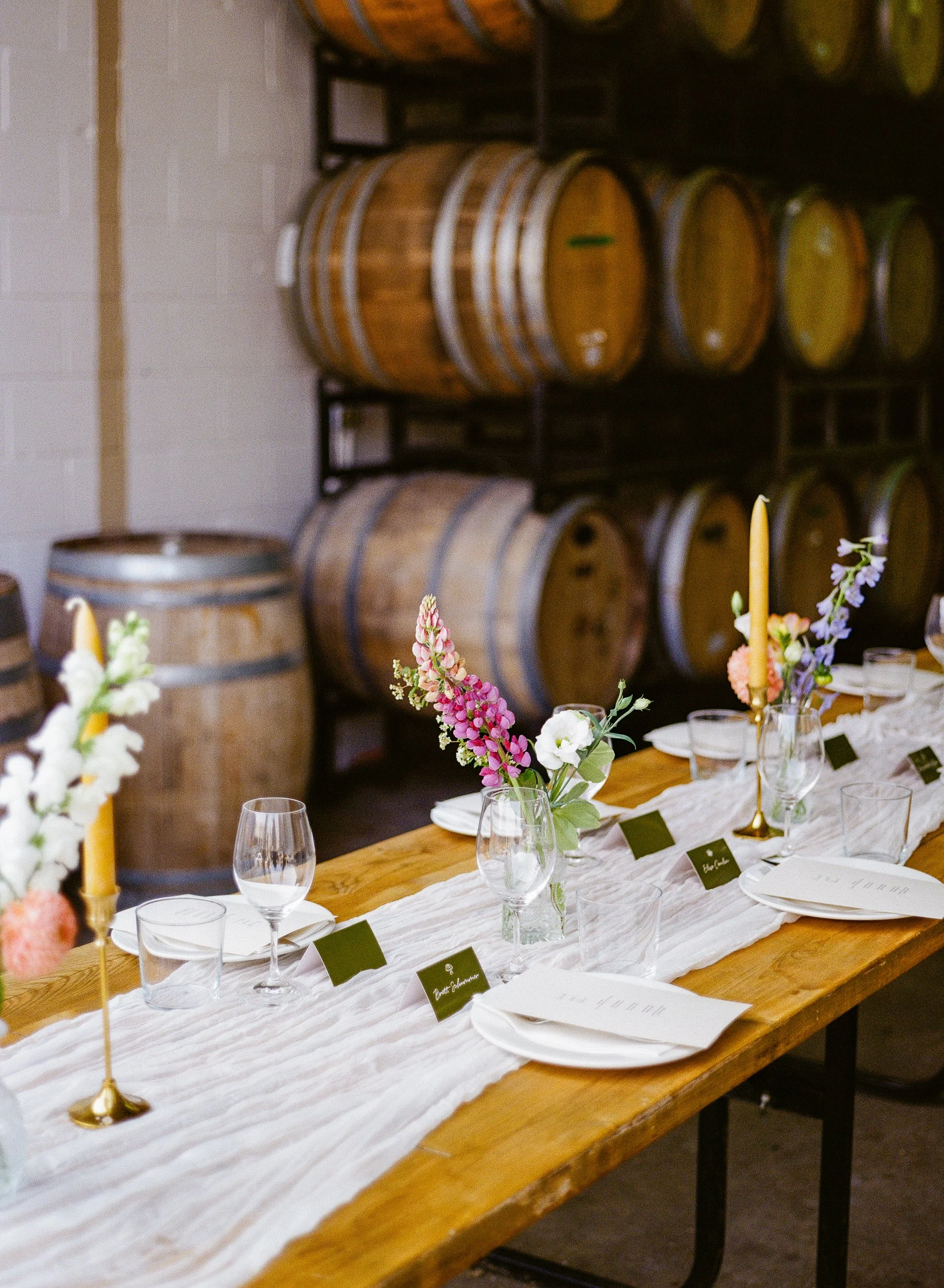 A dining table with a white table runner, floral centerpieces, wine glasses, plates, name cards, and menus.