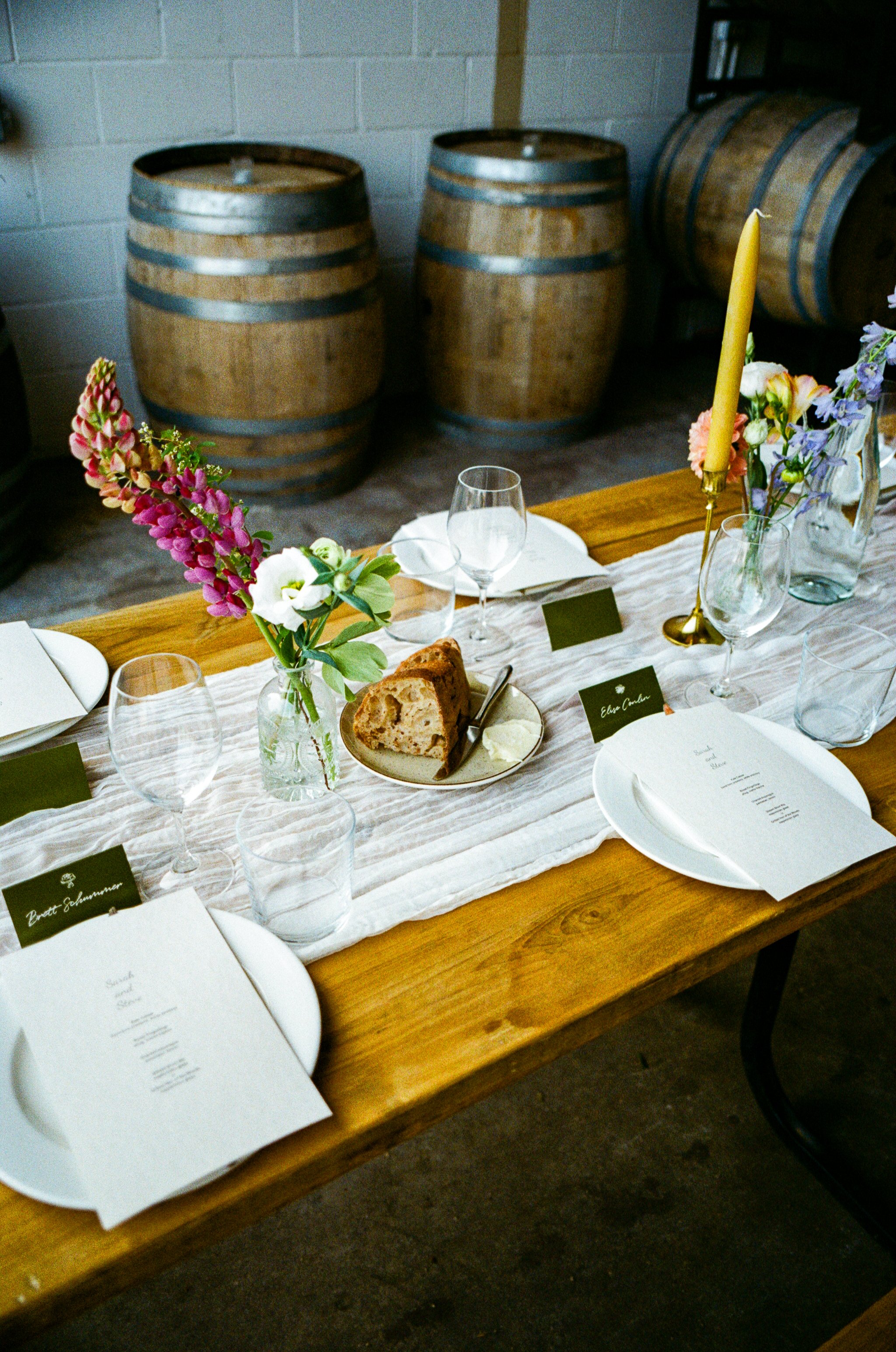A dining table with a white table runner, floral centerpieces, wine glasses, plates, name cards, and menus.