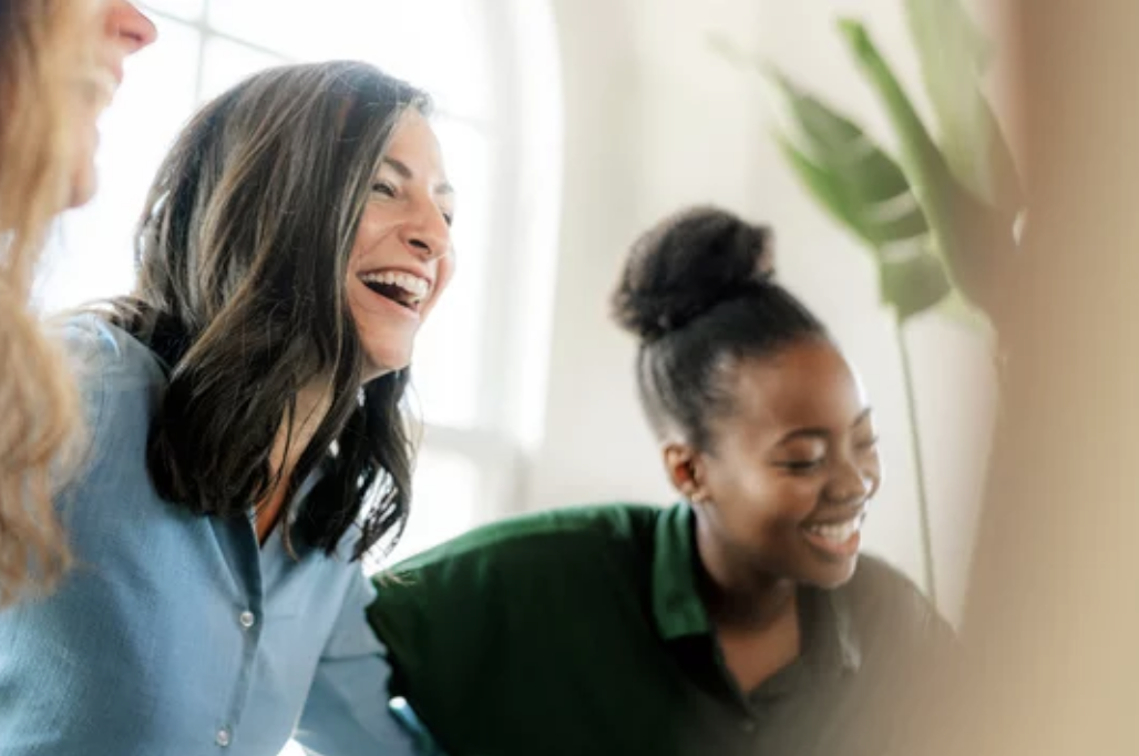 Group of diverse women smiling and laughing together in a bright indoor setting.