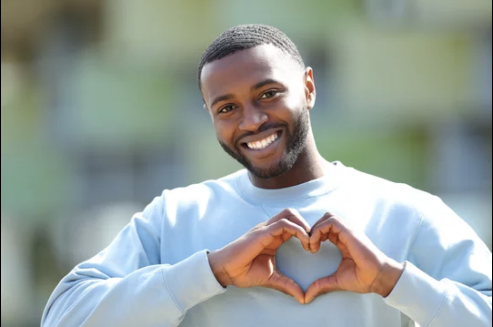 Smiling man outdoors making a heart shape with his hands.