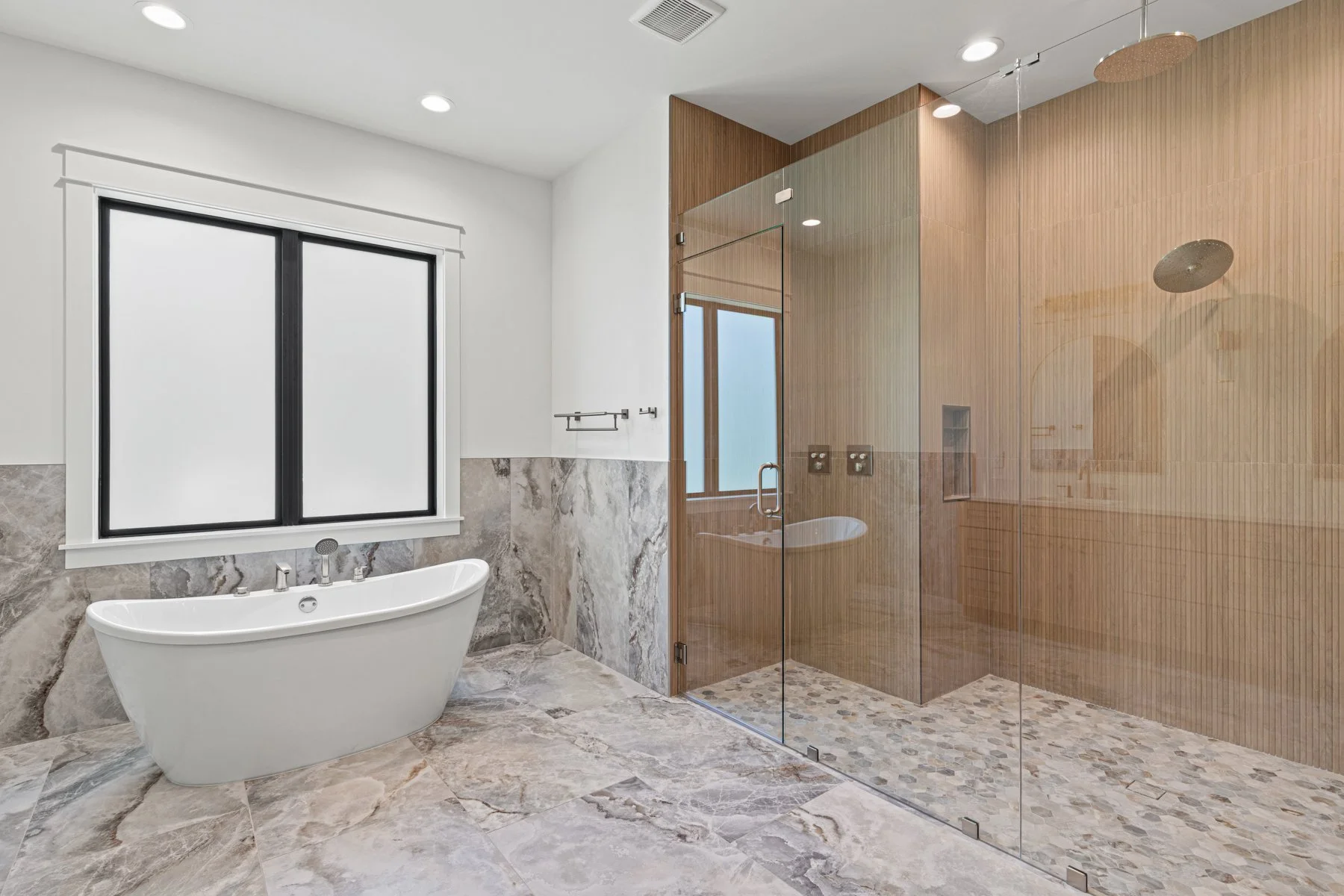 Modern bathroom with a freestanding bathtub, a large window, marble flooring, and a glass-enclosed shower with wood-paneled walls.