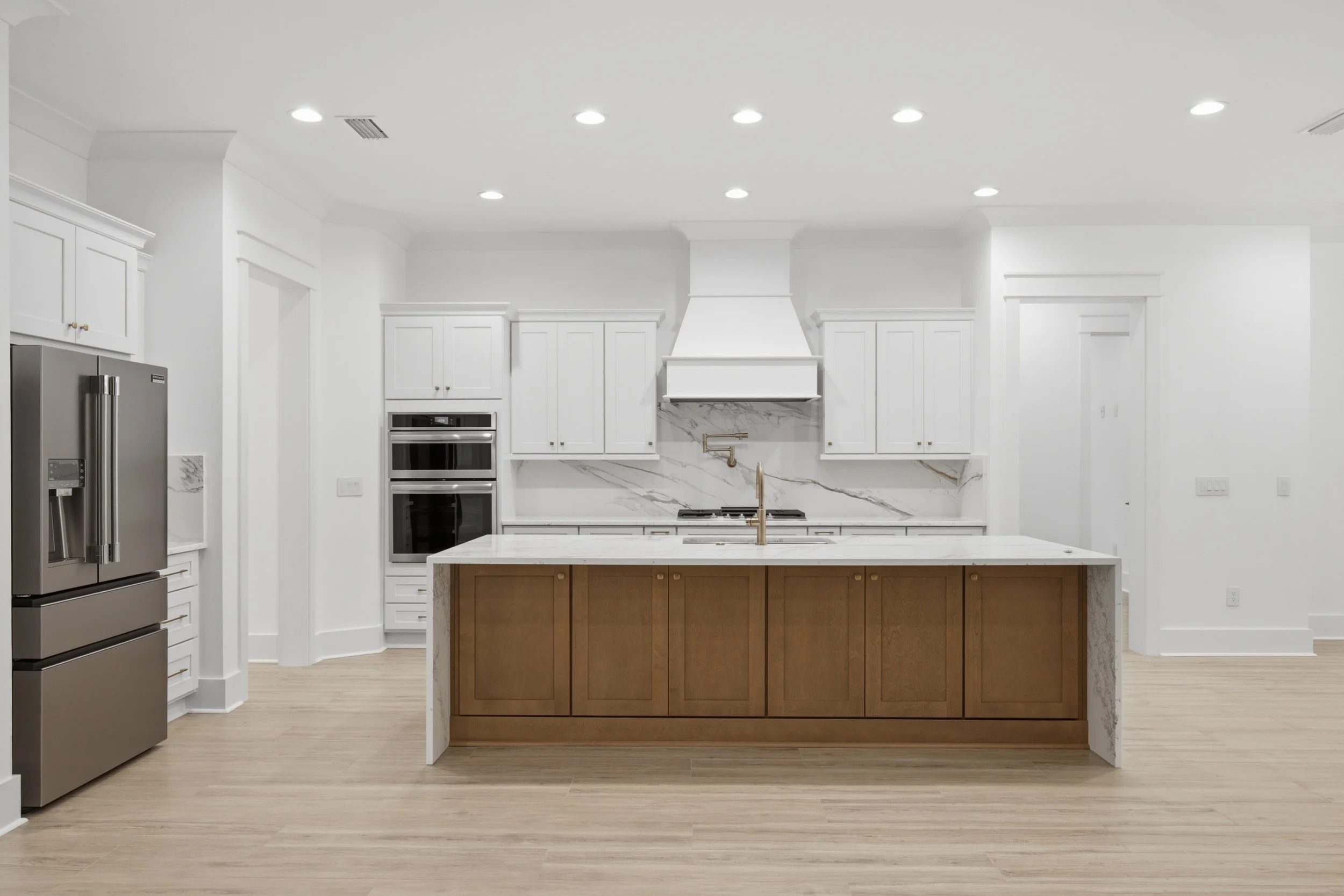 Modern white kitchen with island, stainless steel refrigerator, oven, and quartz backsplash.