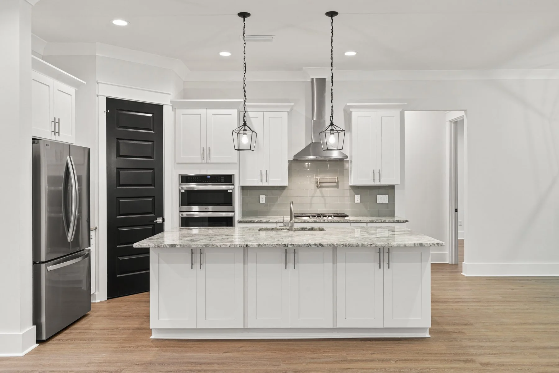 Modern kitchen with white cabinets, stainless steel appliances, a granite island, pendant lights, and light wood flooring.
