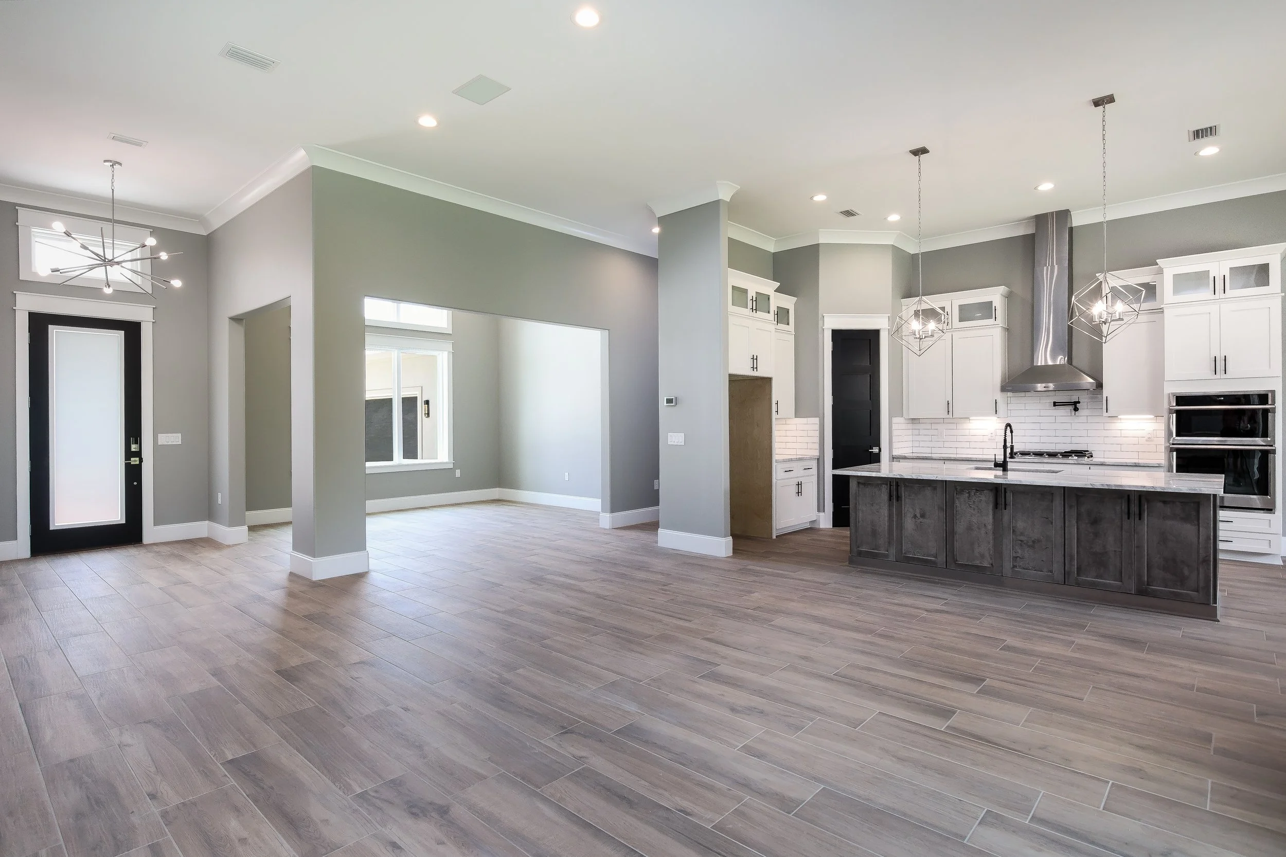 Open-concept kitchen and living area with gray walls, white cabinets, modern light fixtures, and wood-look tile flooring.