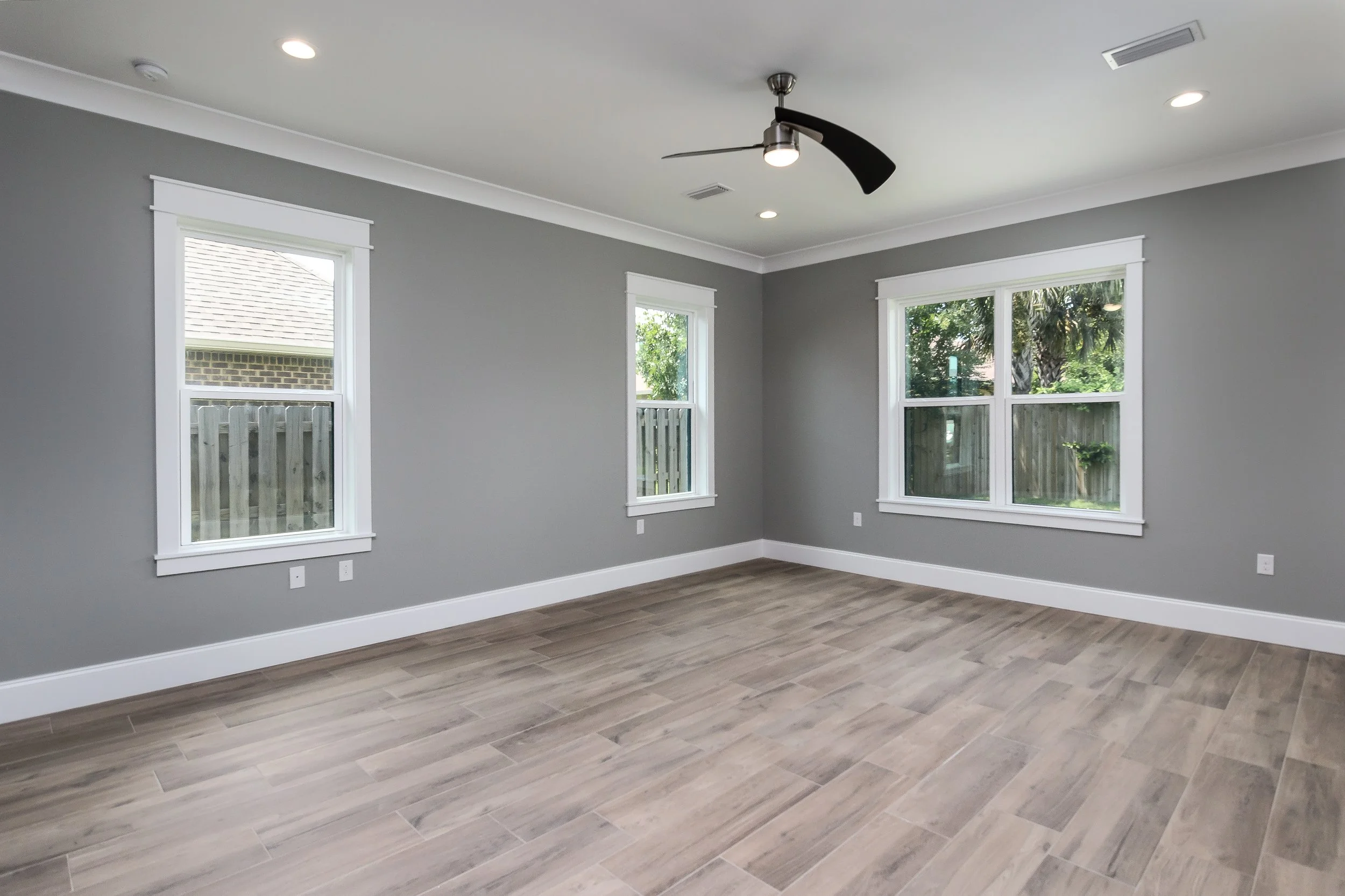 Empty room with three windows, gray walls, white trim, and wood flooring.