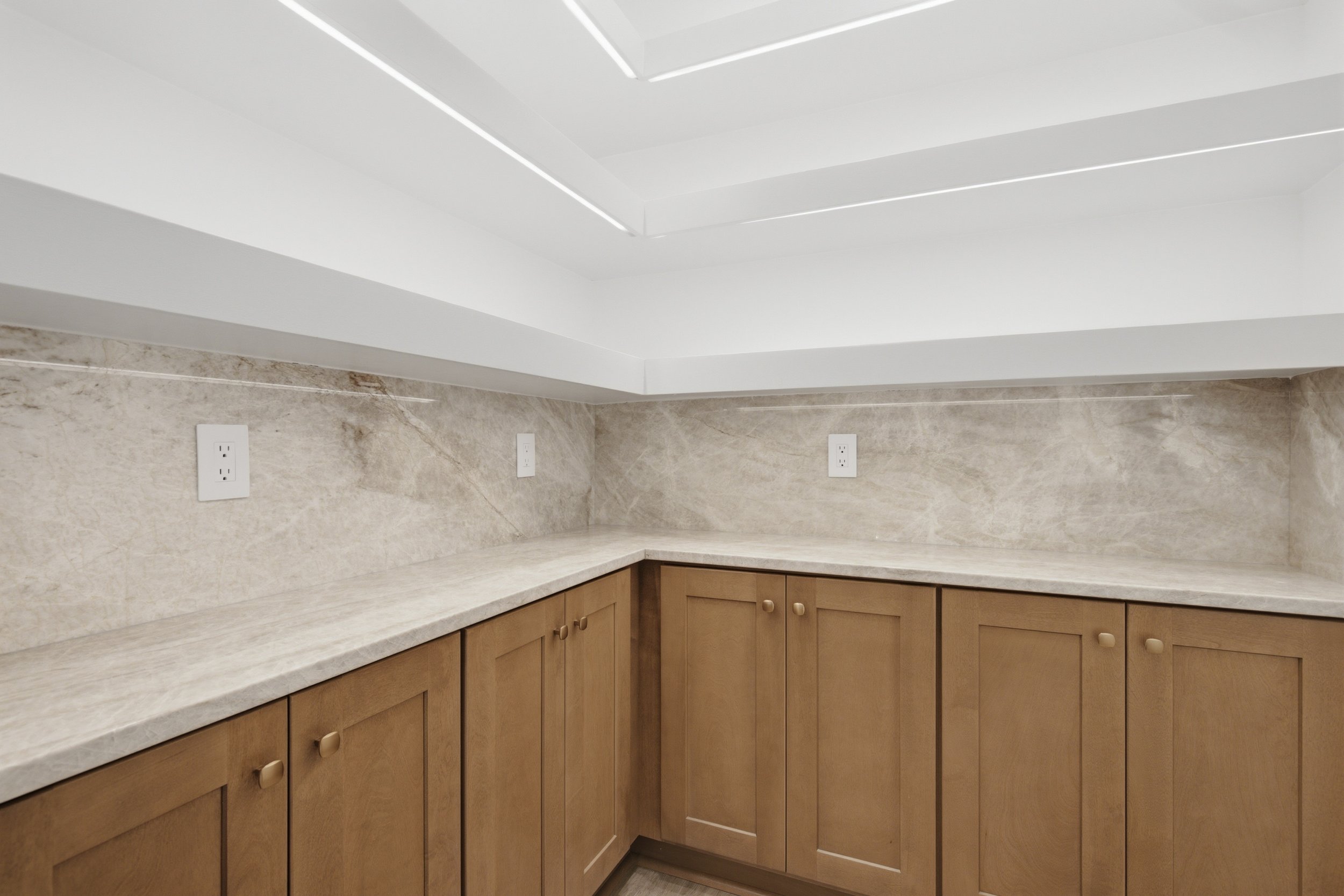 Kitchen corner with beige cabinets, marble countertops, and a marble backsplash. There are three white electrical outlets on the wall.