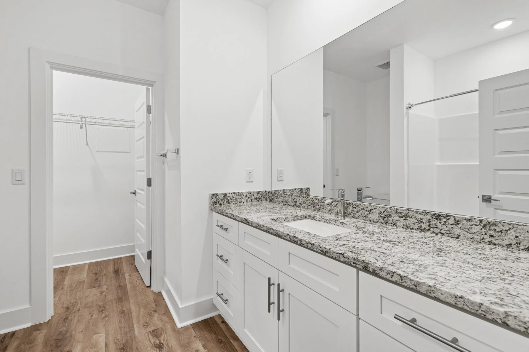 Bathroom with white cabinets, granite countertop, large mirror, and walk-in closet in background