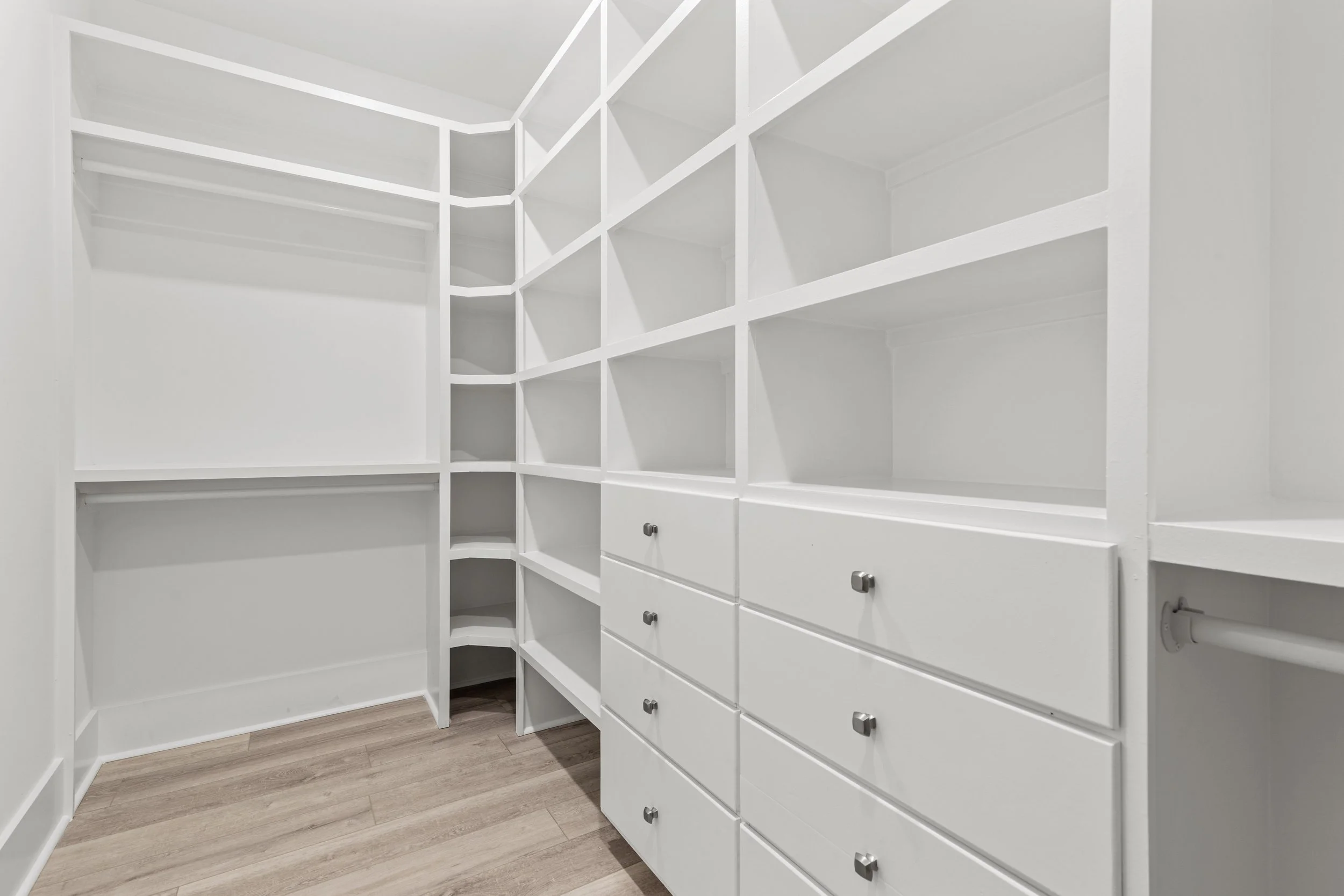 Empty white built-in shelves and drawers in a closet with wood flooring.