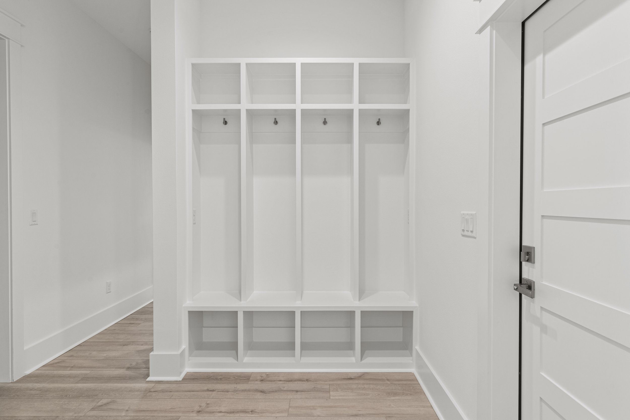 Empty white cubby storage unit with hooks inside, located in a room with white walls and wood flooring.