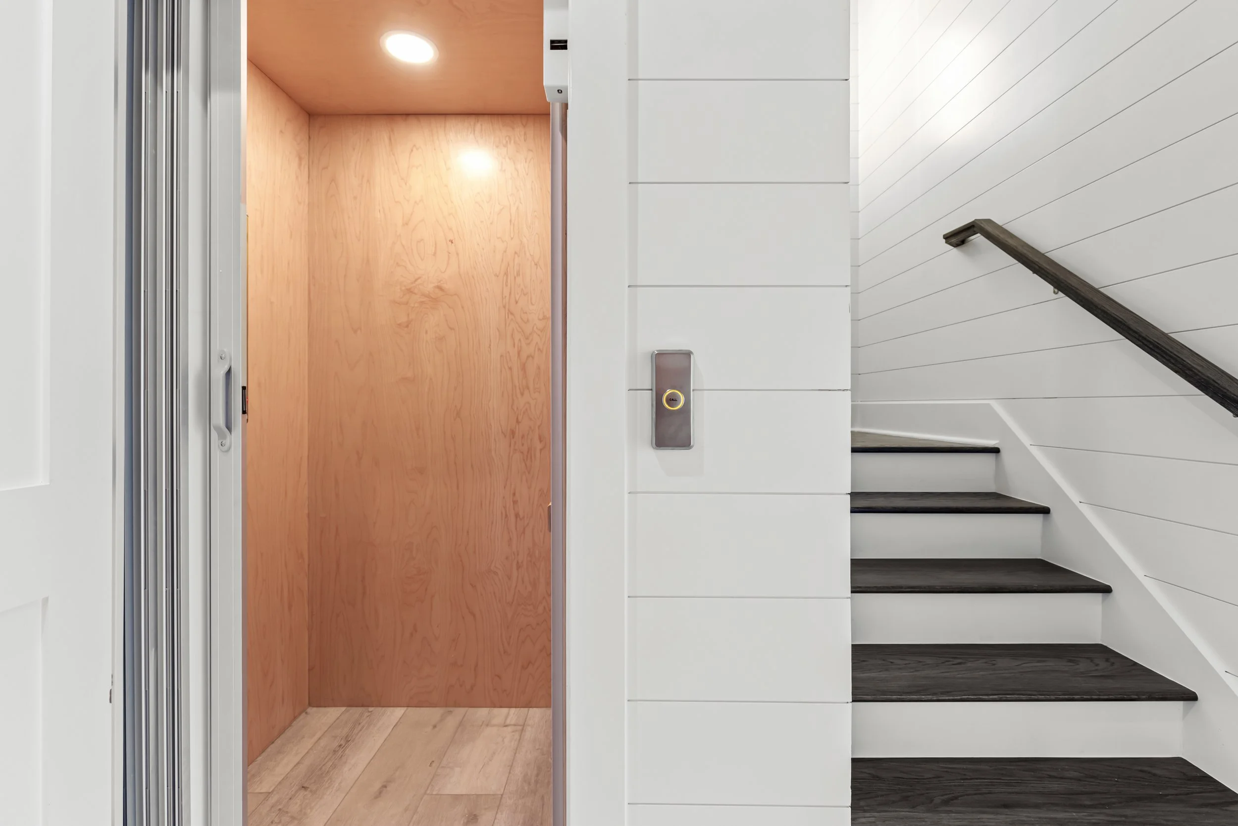 View of an elevator interior with a wooden panel door, a ceiling light, and a button panel.