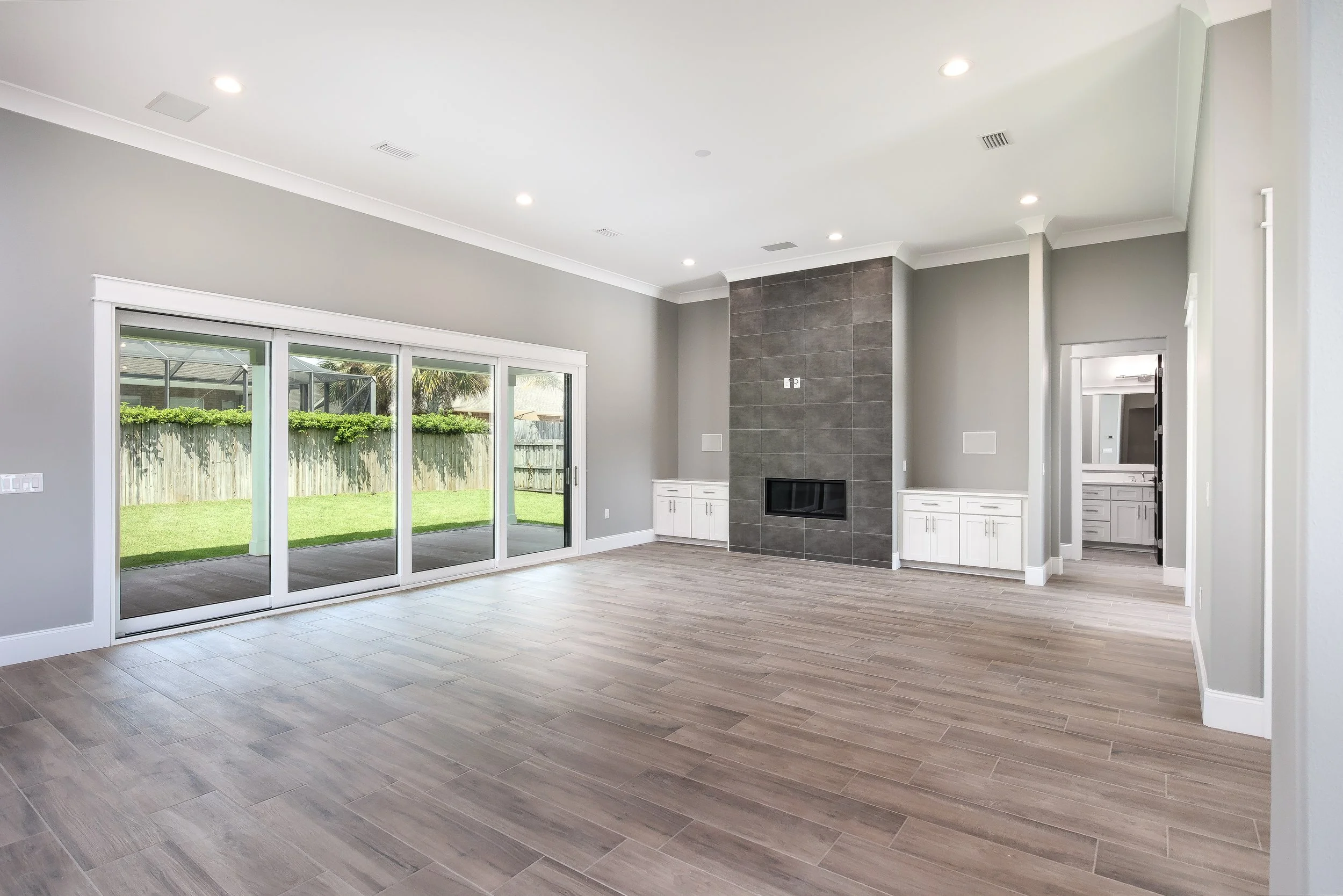 Bright living room with light wood flooring, large sliding glass door leading to backyard, gray walls, white trim, and a fireplace with gray tile surround.