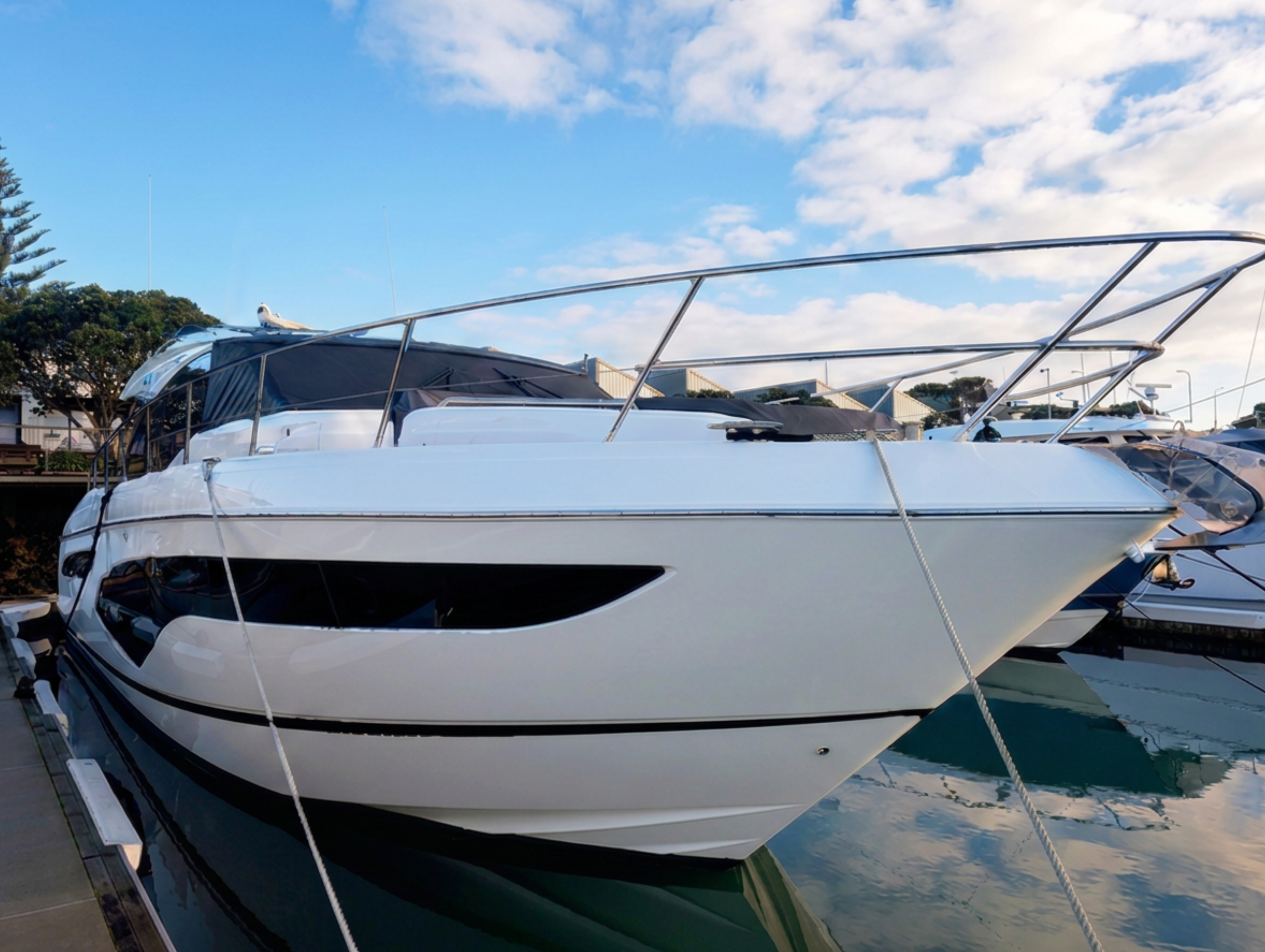 Multiple white yachts docked at a marina with a background of blue sky and scattered clouds.
