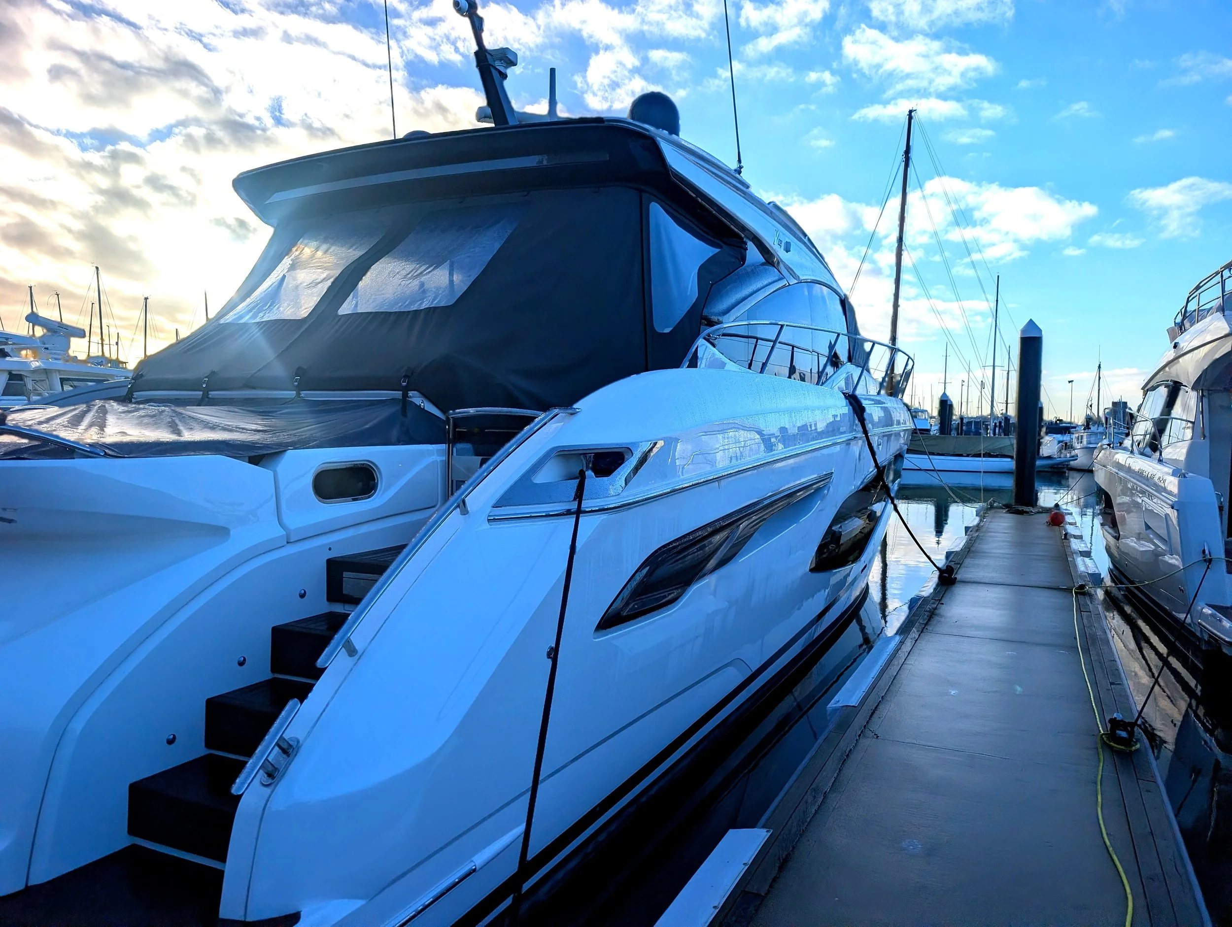 A docked yacht with a black and white exterior, surrounded by other boats at a marina under a partly cloudy sky.