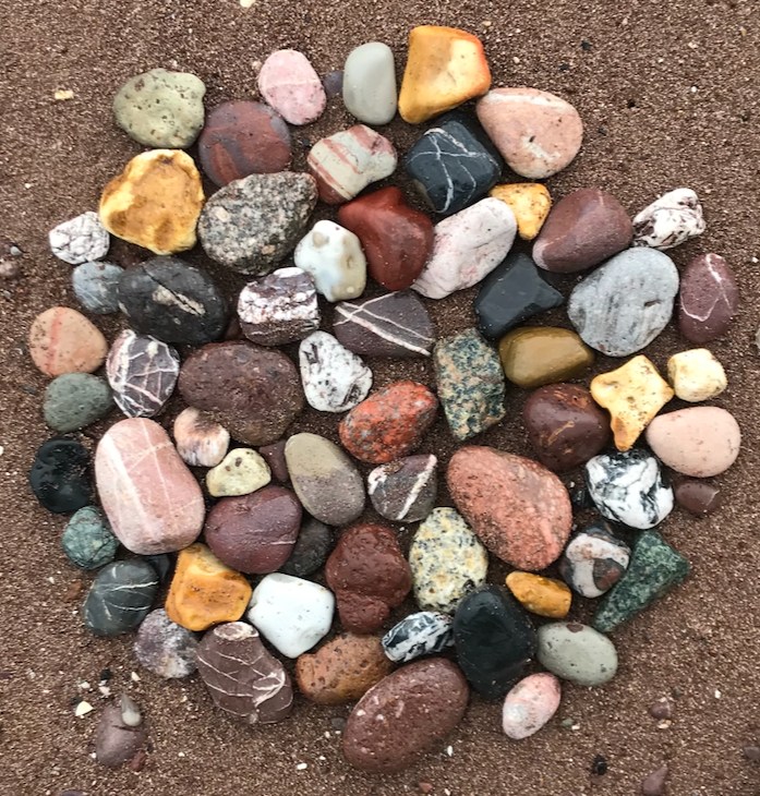 Collection of various small, colorful stones and pebbles  on a sandy beach ground