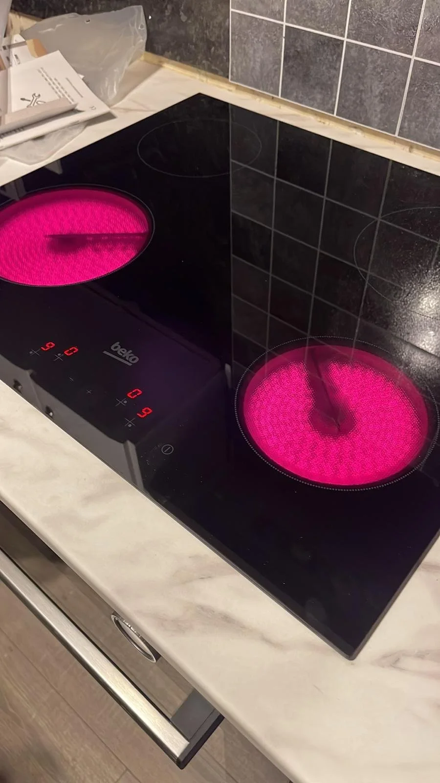 Electric stovetop with two hot pink glowing burners in a kitchen with tiled walls and a marble countertop.
