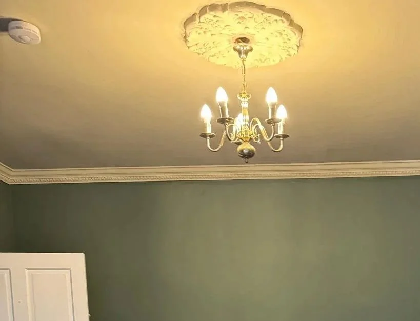 A ceiling with a decorative chandelier hanging from a ceiling medallion in a room with green walls.